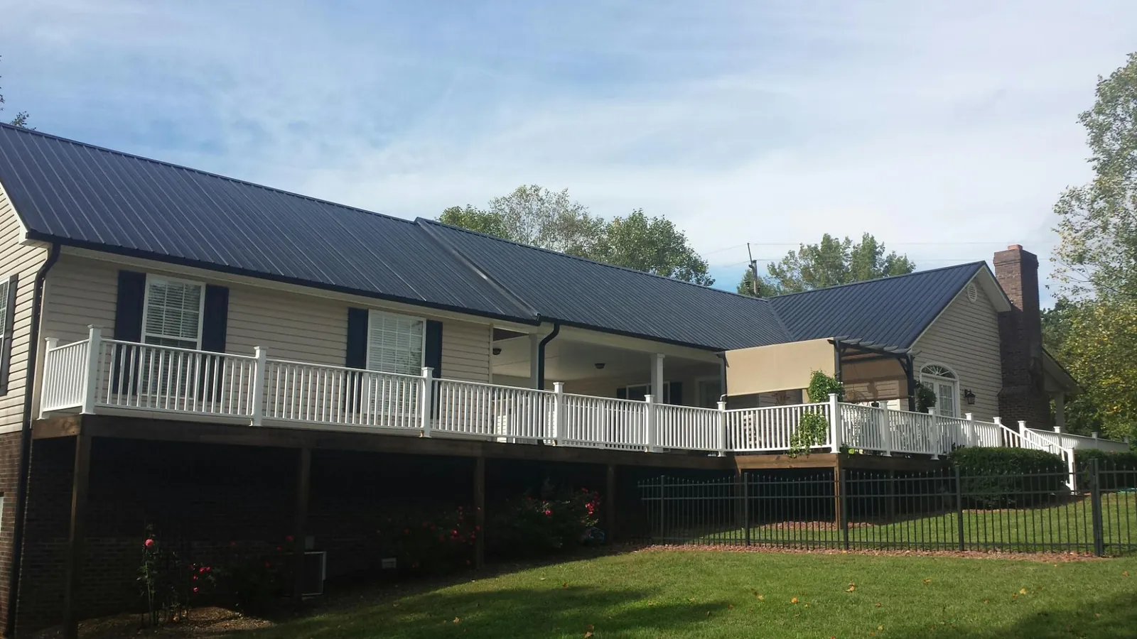 Black metal roof above a long white railed deck on a hillside home in Wellsville