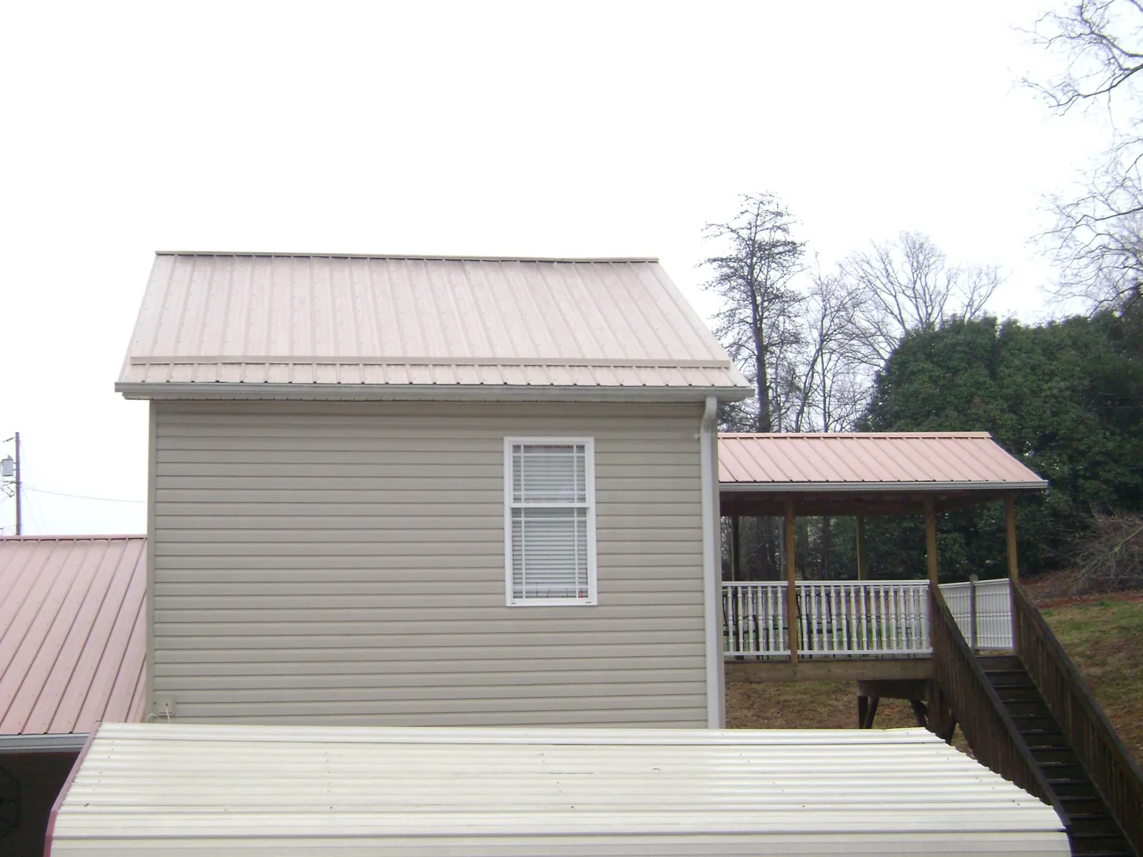 Tan metal roofs on a two story addition and attached porch, from a Roof Replacement job in Wellsville