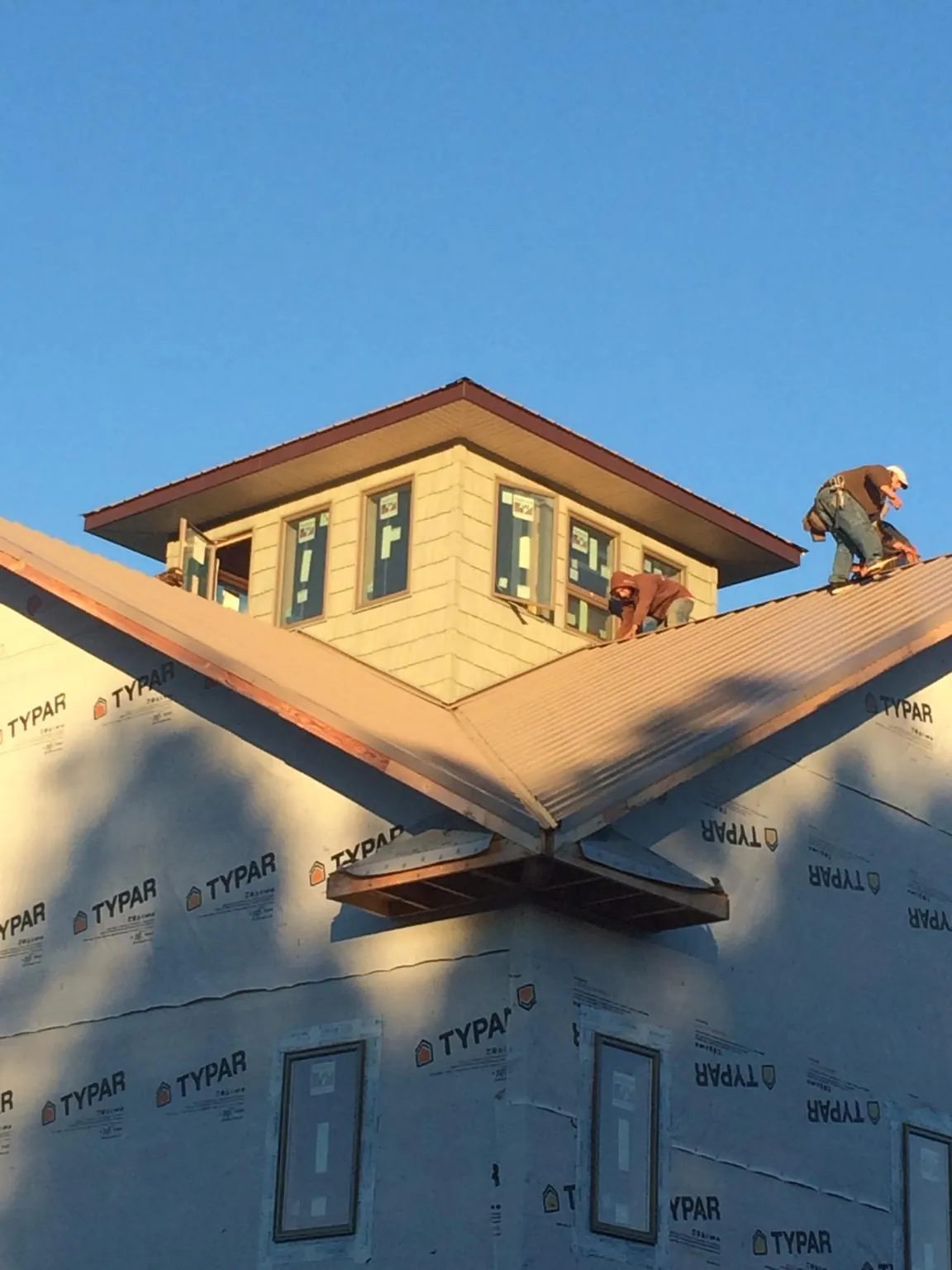 Roofers working around a rooftop cupola on a new metal roof at sunset — Roof Waterproofing in Wellsville by Roofing Brothers